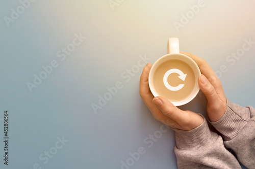 A cup of coffee in the hand of a person with a reboot icon. Coffee break symbol