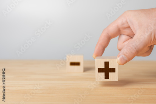 Wooden cubes with the image of pros versus cons. erson Holding Plus Sign Block Against Minus. hand choose wood cube with plus and minus on gray background, copy space.