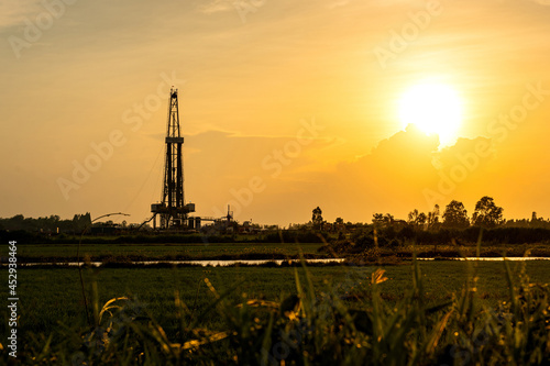 Silhouette black shadow of oil exploration drilling rig structure among the orange sunrise sky and agriculture field environemnt. Energy industrial background photo.