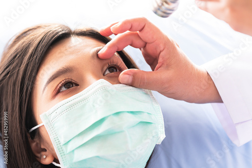 Doctor checking the eyes of a woman patient, which wearing a surgical mask, to people health care and Cataract disease concept.