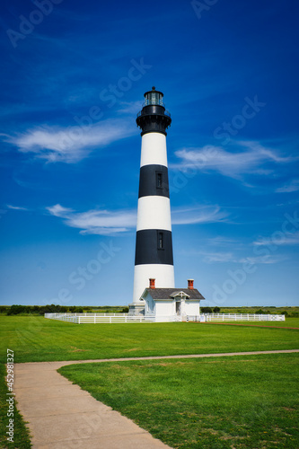 A vertical landscape of the Bodie Island Lighthouse front view under a cloudy blue sky.