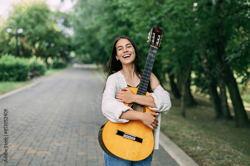 A charming guitarist hugs her favorite instrument during a walk in the summer park. Summer time, music, musician