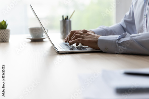 Hands of office employee typing on laptop keyboard at workplace. Business man working at computer, using online app, chatting, browsing internet, writing article or report. Close up, cropped shot