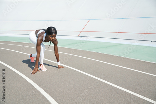 Beautiful young African woman standing at starting position on running track outdoors