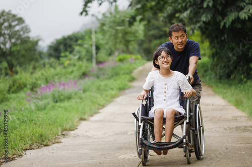 Father and Disabled child on wheelchair walking on trail park in sunny day. Happy disability kid travel in family holiday concept.