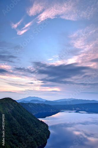 雄大な夜明けの空を湖面に映す山間の湖。日本の北海道の摩周湖。