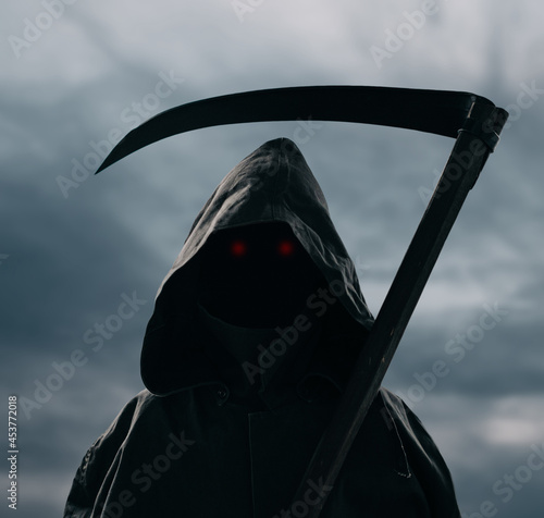 Death with a scythe stands against the background of a gloomy sky.