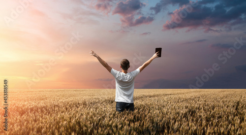 man holding up Bible in a wheat field