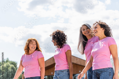 Cheerful multiethnic women with pink ribbons walking outdoors