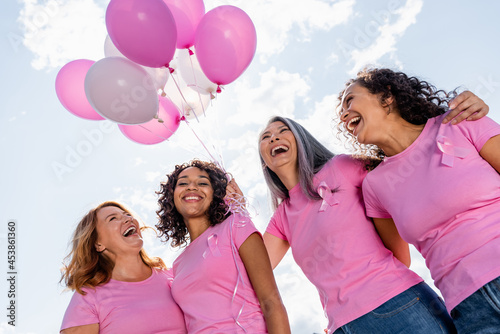 Low angle view of happy multiethnic women with ribbons of breast cancer awareness and balloons outdoors