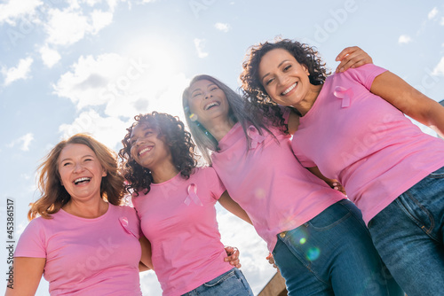 Low angle view of cheerful multicultural women with pink ribbons hugging outdoors