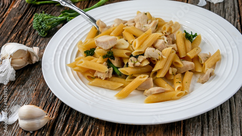 Penne pasta with chicken, garlic and brocolii on rustic wooden table