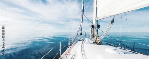 White sloop rigged yacht sailing in an open Baltic sea on a clear sunny day. A view from the deck to the bow, mast and sails. Estonia