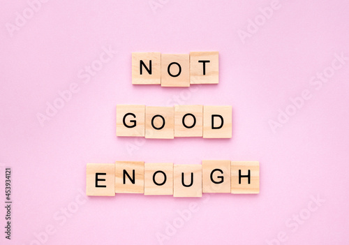 Phrase 'not good enough' on wooden blocks on pink background