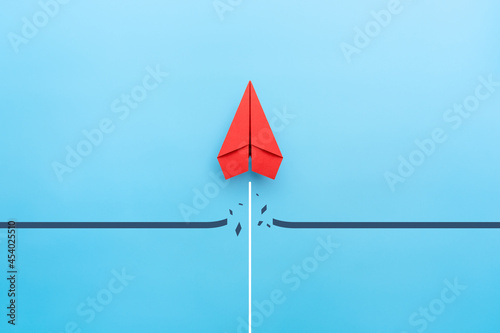 Red paper plane breaking through obstacle on blue background, Concept of overcoming barriers, goal, target