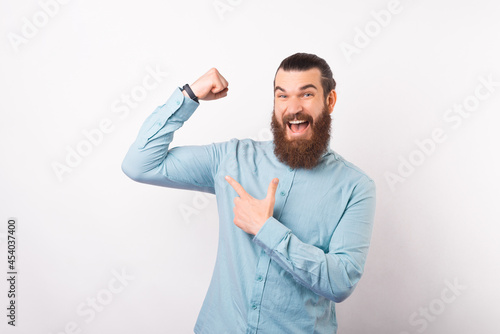 Young business man is holding up his arm while pointing at his biceps over white background.