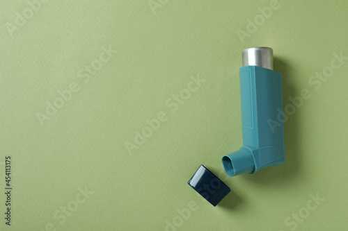 Blue asthma inhaler on green background, top view