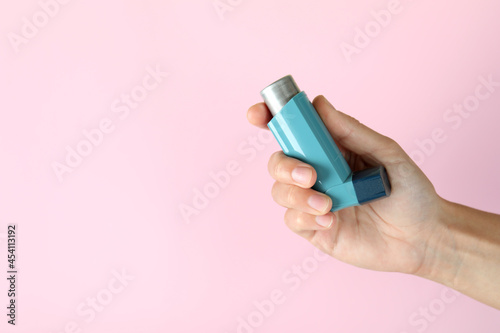 Female hand holds asthma inhaler on pink background