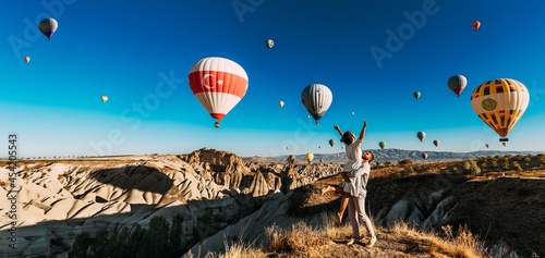 A happy couple among balloons in Cappadocia. A couple in love against the background of flying balloons in Cappadocia. Travel to Turkey. Balloons in the sky, panorama. Wedding trip. Honeymoon trip
