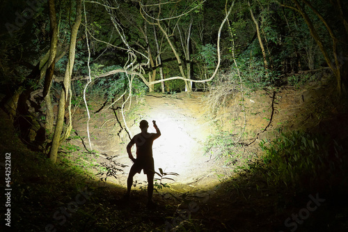 A trail runner using a flashlight in dark forest