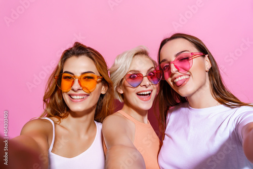 Self portrait of three funny, funky, emotional, expressive, pretty girls, gesture posing on pink background, celebrating birthday, women's day, spring