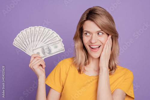 Photo of young pretty woman happy positive smile shocked hold dollars win lottery isolated over violet color background