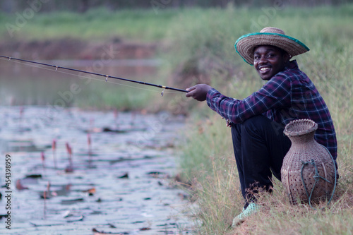 African fisherman happily catches a rod by a pond in a rural area.