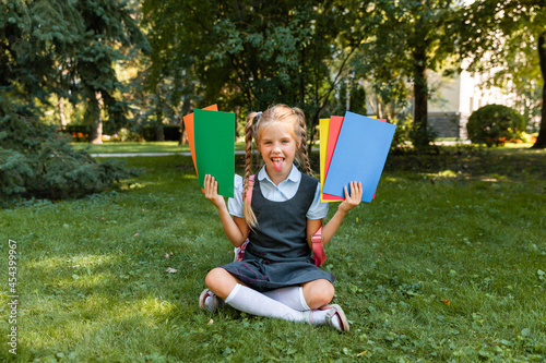Education concept. Cute smiling schoolgirl sitting on the grass. Happy little girl holding books