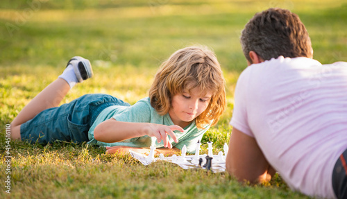 happy family of dad and son child playing chess on green grass in park outdoor, tactic