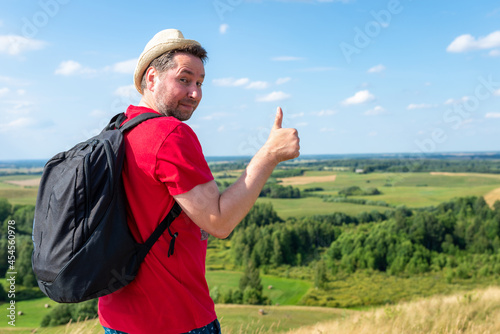 Cheerful travel man showing thumb up. traveler with straw hat shows thumb up against beautiful summer valley.Copy space