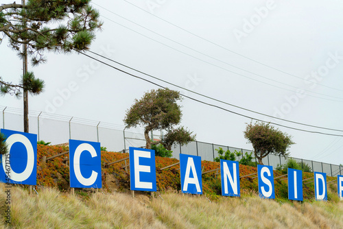 Scenic view of oceanside signage on a hill under a cloudy sky