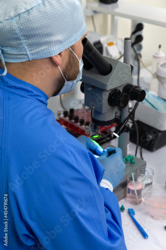 A male scientist in a mask looks through a microscope in a laboratory.