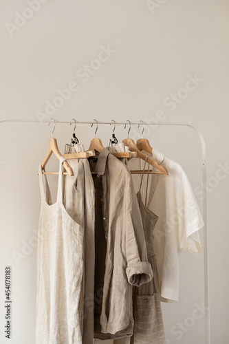 Women's aesthetic minimal fashion pastel clothes made of washed linen. Stylish female blouses, dresses, pants, shirts on hanger on white background. Fashion blog, website, social media
