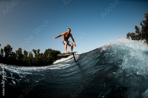 adult man riding on the wave with hydrofoil foilboard on background of blue sky