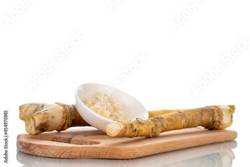 Two whole spicy horseradish roots and grated horseradish in a white saucer, close-up isolated on white.