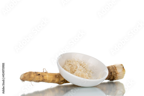One whole spicy horseradish root and grated horseradish in a white saucer, close-up isolated on white.