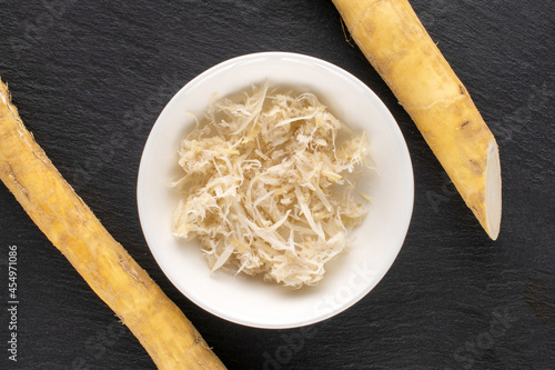 Grated horseradish roots in a white saucer on a stone from slate, close-up, top view.