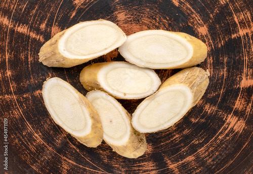 One horseradish root cut into slices on a clay plate, close-up, top view.