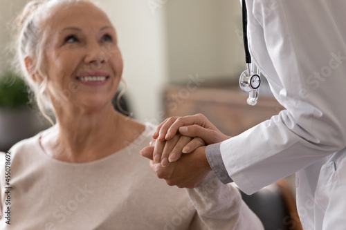 Happy senior woman visiting doctor, getting optimistic news after medical checkup, therapy. Therapist holding hand of old patient, giving hope, support, congratulating on goor treatment result