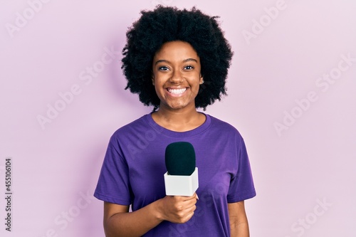 Young african american woman holding reporter microphone smiling with a happy and cool smile on face. showing teeth.