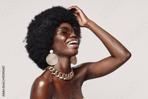 Beautiful young African woman in golden jewelry keeping eyes closed and smiling