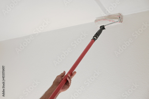 Hand of a man holding a paint roller on a long telescopic pole to paint the ceiling while renovating an apartment, housing concept, copy space, selected focus