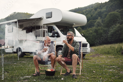 Mature man with senior father talking at campsite outdoors, barbecue on caravan holiday trip.