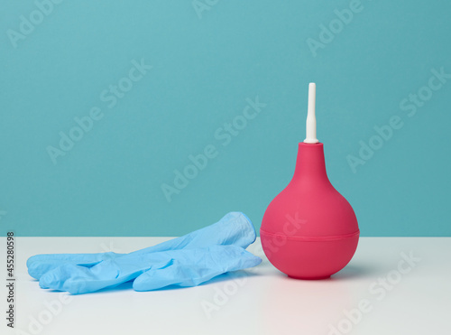 pink rubber enema on white table, medical instrument for cleaning the body, blue background