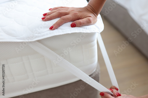 Woman puts blanket or mattress topper on bed closeup