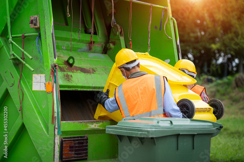 Rubbish cleaner man working with green garbage truck loading waste and trash bin at city,Waste collectors at work.