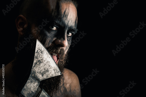 Viking warrior with black war paint, licking his axe.