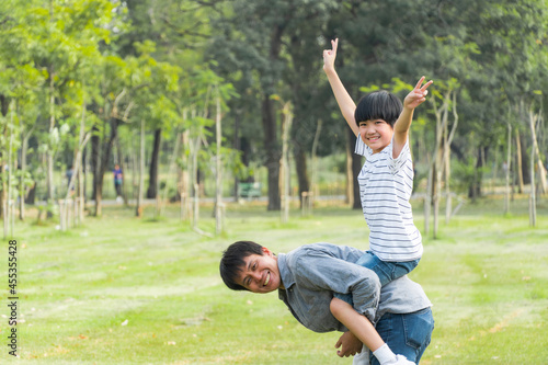 Asian father piggyback his son. Little boy raising arms up in the air. family support and playing together. superhero pose. copy space