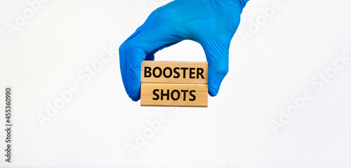 Covid-19 booster shots vaccine symbol. Doctor hand in blue glove holds wooden blocks with words booster shots, beautiful white background. Covid-19 booster shots vaccine concept.