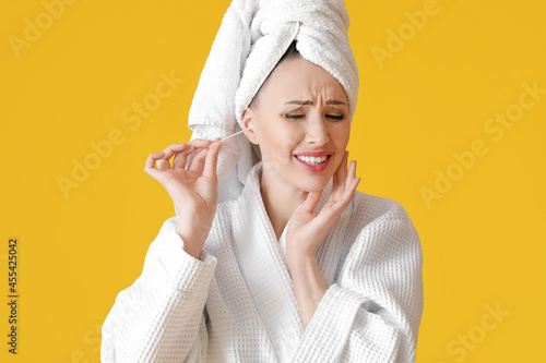 Young woman cleaning ears with cotton bud on color background